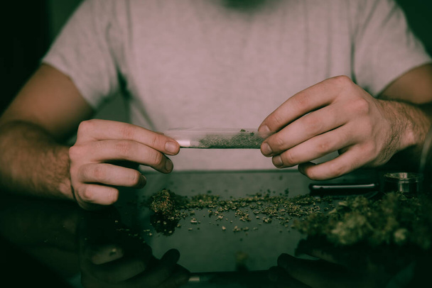 Közelkép a függőkről, akik öngyújtóval gyújtják meg a marihuánát. Egy férfi marihuánát gurít. Droghasználat. Drogos fogalom. Közelről. Ember előkészítő és gördülő marihuána cannabis joint. - Fotó, kép