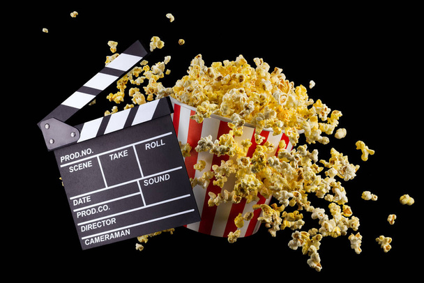 Flying popcorn and film clapper board isolated on black background, concept of watching TV or cinema. - Valokuva, kuva