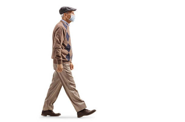 Volledig profiel foto van een mannelijke gepensioneerde lopen en dragen van een beschermende medische masker geïsoleerd op witte achtergrond - Foto, afbeelding