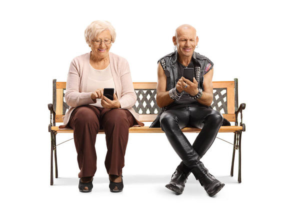 Elderly woman and a punk sitting on a bench and using mobile phones isolated on white background  - Photo, image