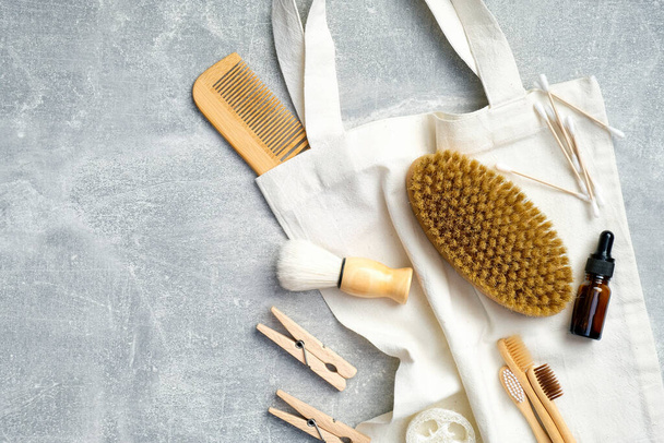 Top view eco-friendly bath accessories with canvas bag on stone table. Flat lay wooden hair comb, brush, essential oil, loofah sponge, bamboo toothbrushes. SPA treatment at home, body care - Foto, Imagen