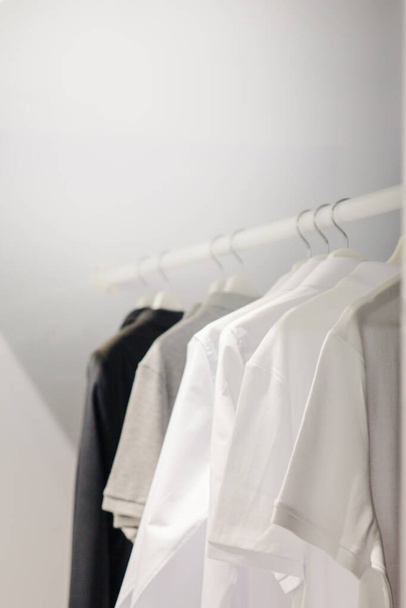 Camisetas blancas colgando en la cómoda, negro, tela gris en clothet, lavandería limpia espacio de copia de fondo blanco
 - Foto, Imagen