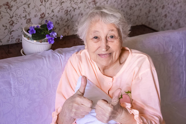 Die glückliche Seniorin im Bett mit dem Zeichen ok - Coronavirus Covid-19 Genesungskonzept. Gesundheits-, Sicherheits- und Pandemiekonzepte - Foto, Bild