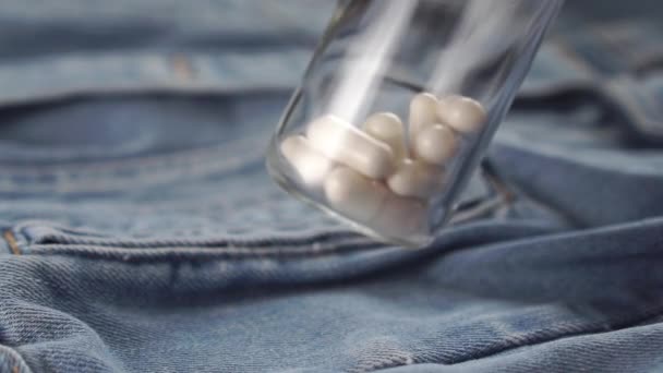 bottle with white capsules shakes over blue denim clothes. Slow motion. Close-up. The concept of the use of stimulants for the treatment of sexual dysfunction - Záběry, video