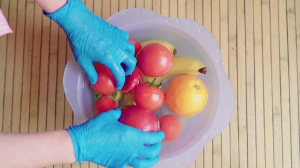 Mujer con guantes de látex azul quitando un lavabo de plástico con agua y lejía en la cocina para limpiar la fruta. Desinfectar las frutas para prevenir la propagación del coronavirus. Fruta con base de madera
 - Metraje, vídeo