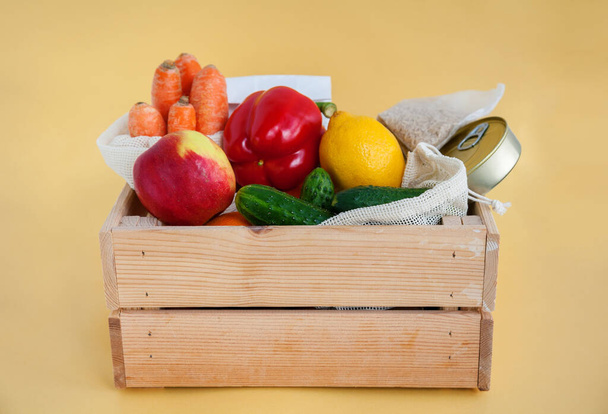 Δωρεά ξύλινο κουτί με διάφορα τρόφιμα. Κονσερβοποιημένα τρόφιμα, δημητριακά, φρούτα, λαχανικά. Κίτρινο φόντο - Φωτογραφία, εικόνα