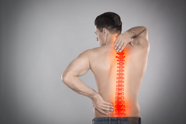 Άνθρωπος που υποφέρει από πόνο στη σπονδυλική στήλη σε γκρι φόντο - Φωτογραφία, εικόνα