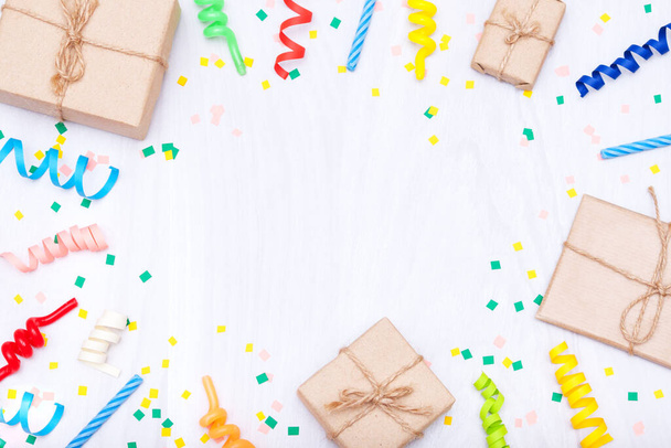 Colorful gifts, confetti, candles, streamers on white wooden background. Flat lay, copy space, holiday frame or background. - Photo, Image