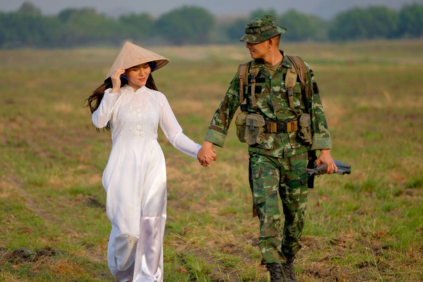 Voják muž drží ruku vietnamské ženy a procházka v poli s večerním světlem v pojetí lásky během války. - Fotografie, Obrázek