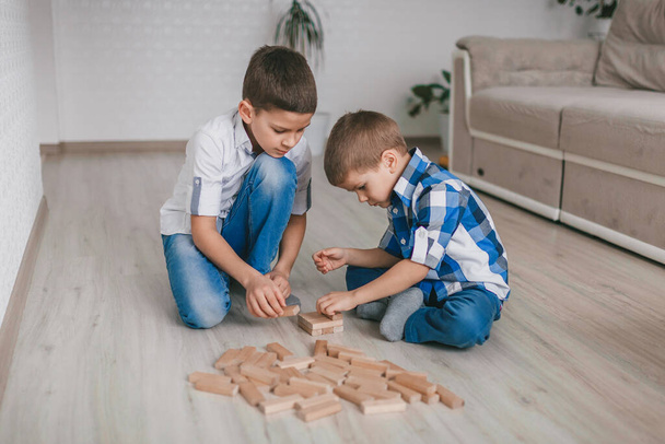 Két testvér fiú épített egy fatornyot a ház fablokkjaiból a padlón. Asztali játék. A független családi karantén, fertőzés, koronavírus, önizoláció fogalma - Fotó, kép