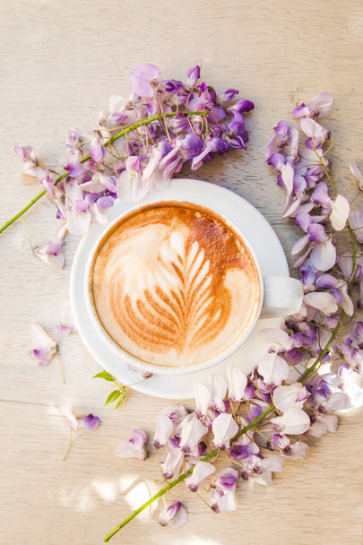 Διακοσμημένος καπουτσίνο καφέ περιτριγυρισμένος από όμορφα ανοιξιάτικα λουλούδια - Φωτογραφία, εικόνα
