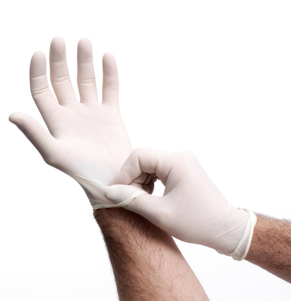 Kıllı kollu tanımlanamayan erkek beyaz arka plana steril lateks eldiven takıyor. - Fotoğraf, Görsel