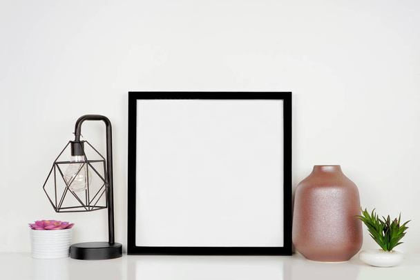 Mock up black square frame with home decor and potted plants. White shelf against a white wall. Copy space. - Фото, изображение