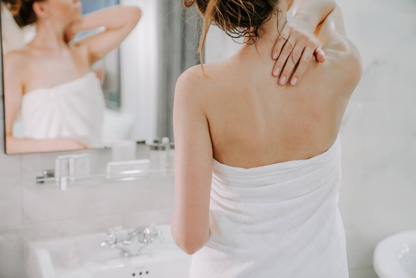 schöne Frau nach der Dusche in einem weißen Handtuch schmiert die Haut mit Creme. Hausgemachte Körperpflege. Wellnessanwendungen - Foto, Bild