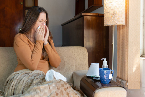 Evindeki kanepede oturup burnunu silen bir kadın. Hasta Hissetme Konsepti. - Fotoğraf, Görsel