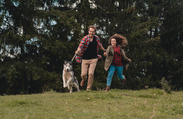 Birbirine aşık çiftler dağlarda köpekleriyle birlikte doğa yolculuklarında el ele tutuşurlar. Gençler birlikte mutlu. Sevgililer tatilde köpekle yürür - Fotoğraf, Görsel