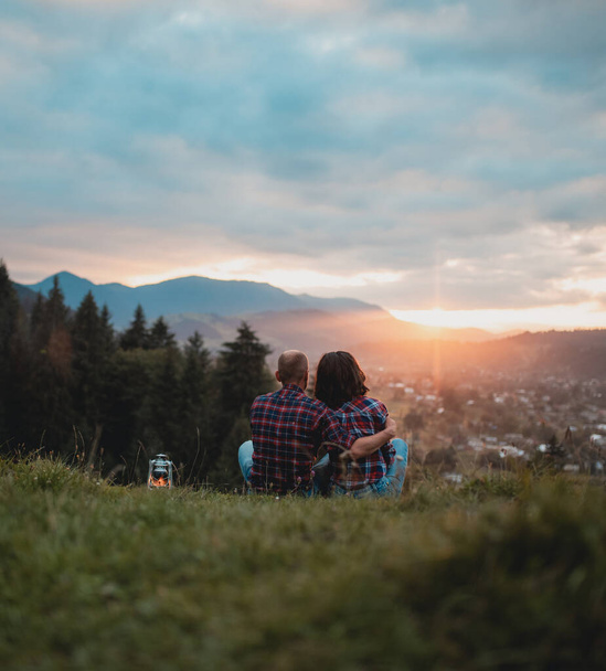 Mann und Frau sitzen auf einem Gras, umarmen sich und schauen weg, Liebe und Gefühle begreifen Familienkonzept, Mann und Frau Beziehungen in den Bergen. Rückseite. - Foto, Bild