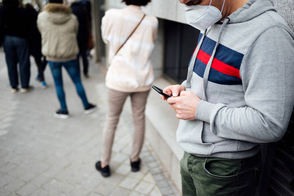 Άνθρωπος που χρησιμοποιεί smartphone σε μια σειρά από ανθρώπους που περιμένουν - Φωτογραφία, εικόνα