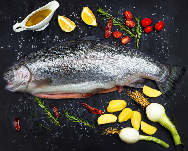 Salmón crudo entero. Pescado fresco con especias, tomates, cebollas, limón, patatas y aceite de oliva
. - Foto, Imagen