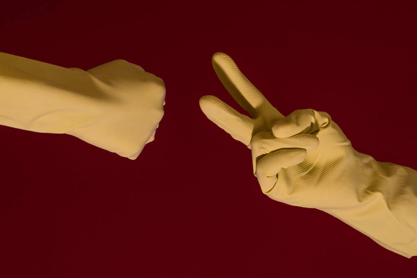 Handen met gele handschoenen die steen papier of schaar spelen in tijd van het coronavirus. Foto met kopieerruimte. - Foto, afbeelding
