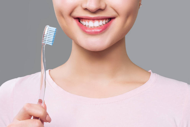 Девушка со здоровыми белыми зубами держит зубную щетку и улыбается. Концепция гигиены полости рта
 - Фото, изображение