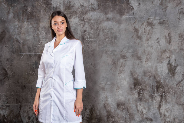 Portrait of attractive young female doctor in white medical jacket on a grey background. Copy space.  - Valokuva, kuva