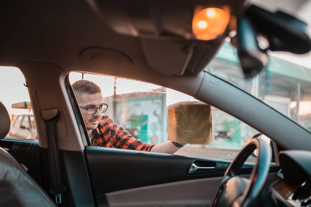 Mladý muž pečlivě čistí vnitřek svého auta hadrem. - Fotografie, Obrázek