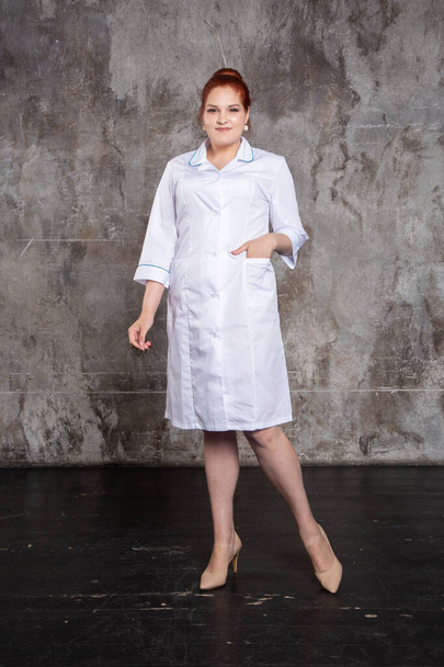 Full length studio portrait of attractive young female doctor in white medical jacket on a grey background. - Photo, Image