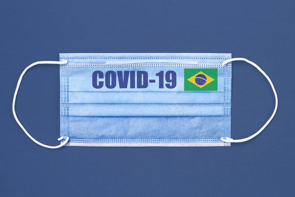Máscara médica y texto o inscripción Covid-19. Concepto pandémico del Coronavirus. Bandera de Brasil
. - Foto, Imagen