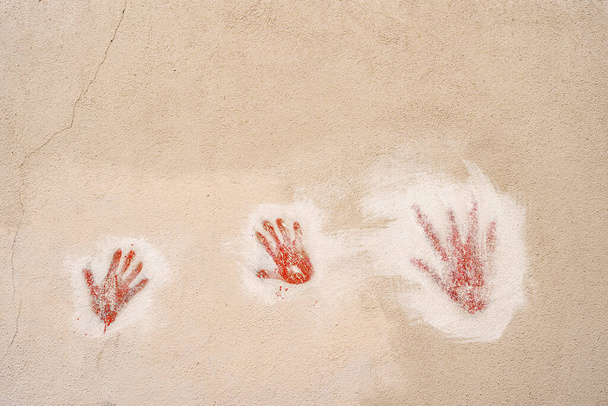 Red handprints on the wall. Two childrens handprints and one adult handprint on a stone wall - 写真・画像