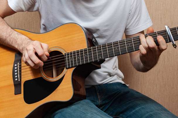 A young European man without a face with jeans and a white T-shirt plays on an acoustic guitar - Photo, Image