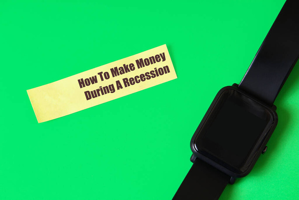 Sticker met de inscriptie of tekst: "Hoe om geld te verdienen tijdens een recessie" op een groene achtergrond met een slim horloge - Foto, afbeelding