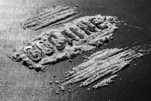 Closeup to Cocaine black lettering in middle of white cocaine with lines over black background. - Fotoğraf, Görsel