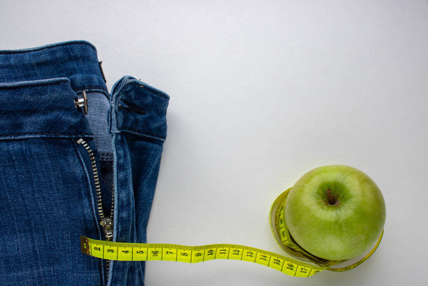 Calça jeans azul, uma maçã verde e um centímetro em um fundo branco.Perda de peso e o conceito de perda de peso
 - Foto, Imagem