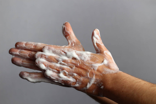 Αρσενικό σαπουνισμένα χέρια σε ένα ανοιχτό γκρι φόντο μπάνιο. Έννοια υγιεινής - Φωτογραφία, εικόνα