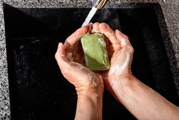 Fehér kézmosás szappannal a víz nyomása alatt. Közelkép zöld borsóval levesből  - Fotó, kép