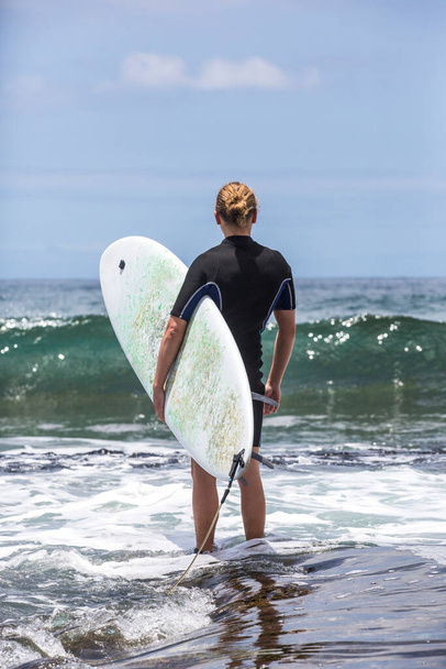 Серфинг входит в воду. Мужчина-сёрфер входит в море со своей доской в черном серфинг-костюме. Тенерифе, Испания
. - Фото, изображение