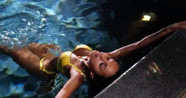 Sexy kobieta w basenie w nocy w żółtym bikini - Materiał filmowy, wideo