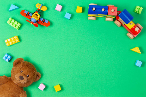 Baby kids educational toys background. Teddy bear, wooden train, red airplane and colorful cubes bricks on light green background. Top view, flat lay - Photo, Image