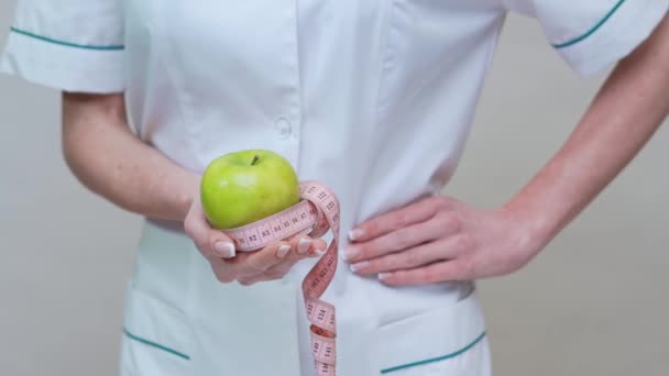 nutritionist doctor healthy lifestyle concept - holding organic green apple and measuring tape - Materiał filmowy, wideo
