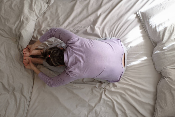 Junge Frau praktiziert Yoga im Sitzen nach vorne beugen Übung, paschimottanasana Pose im Bett. Ansicht von oben - Foto, Bild