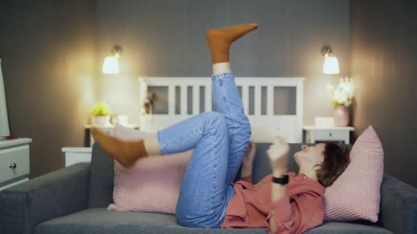 Fröhliche junge Frau liegt auf dem Sofa, guckt Komödienfilm und lacht - Filmmaterial, Video
