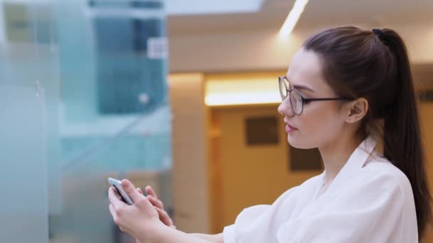 young business lady uses a smartphone. A girl in a white shirt and glasses makes a phone call. - Materiał filmowy, wideo
