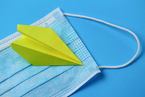 Paper yellow airplane on a blue background with a medical mask - Photo, Image