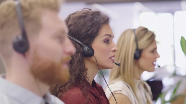 Portrait of confident woman working in a call center while looking at camera. Customer care rappresentative working with team in modern office sitting in a row. Support online with latin call center agent. - Footage, Video