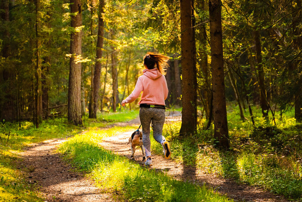 Młoda kobieta i pies biegają razem po lesie. Wesoła kobieta ćwicząca na świeżym powietrzu ze swoim zwierzakiem. Koncepcja osób aktywnych. - Zdjęcie, obraz