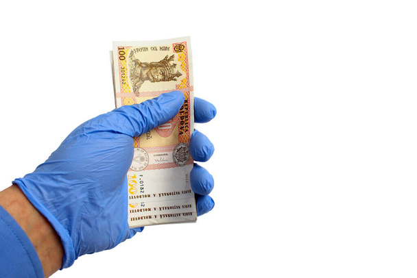 Ένα χέρι σε ένα ιατρικό γάντι κρατά τα χρήματα της πολιτείας της Δημοκρατίας της Μολδαβίας, Lei, σε λευκό φόντο, απομονωμένα. Έννοια του κόστους πανδημίας - Φωτογραφία, εικόνα