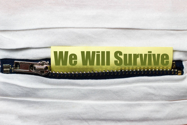 Witte stof met rits close-up. Sticker met tekst of bijschrift: "We zullen overleven" - Foto, afbeelding