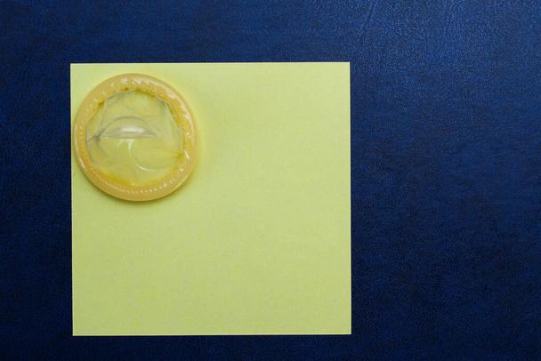 Rozpakowana prezerwatywa i pusta naklejka z miejscem na napis lub tekst na tle skórzanej sofy, stonowana - Zdjęcie, obraz