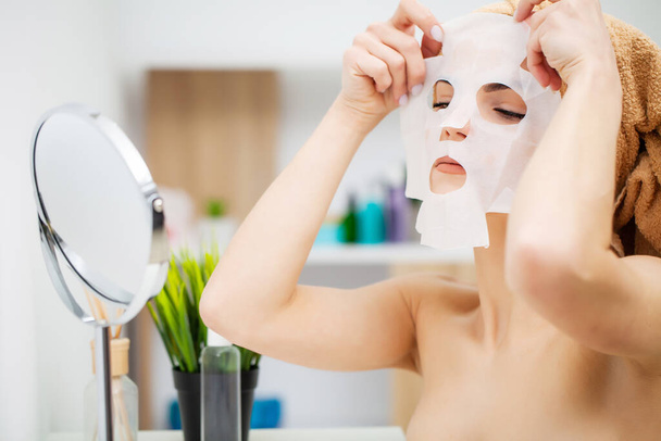 Красива жінка перед дзеркалом кладе маску на обличчя для догляду за шкірою
 - Фото, зображення